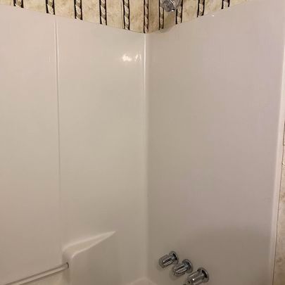 White shower stall with a corner seat, chrome fixtures, and patterned wallpaper border.