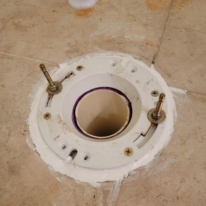 Toilet flange on tiled floor with two bolts inserted, ready for toilet installation.