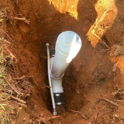 A white PVC pipe and connected parts in a hole in the ground.