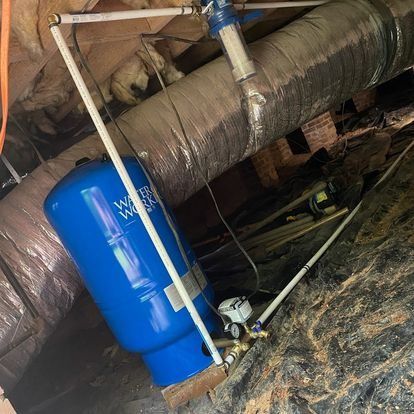 Blue water tank with white pipes, a filter, and gauge in an enclosed space.