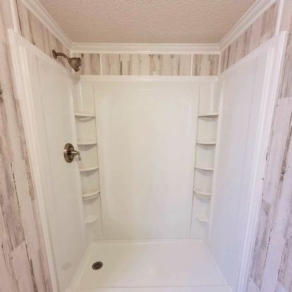 White shower stall with built-in shelves, showerhead, and a drain. Tile-like wall surrounds.