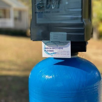Blue water softener tank with black top, business card attached. Outdoors.