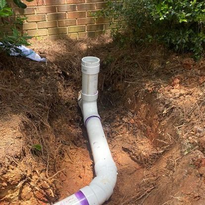 PVC pipes emerging from dirt, near a brick wall and vegetation.