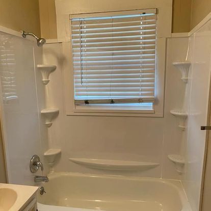 White bathroom with a shower, bathtub, and window with blinds.