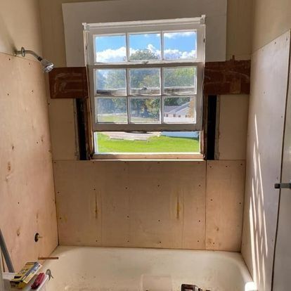 Bathroom under renovation with plywood walls, window, and bathtub.