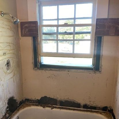 Bathroom renovation with window above bathtub. Partially demolished walls, exposed plumbing, and window frame.