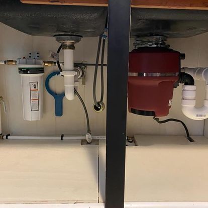 Under kitchen sink: disposal unit and plumbing with water filter, pipes, and sink basin.