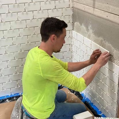 Man tiling a wall with white rectangular tiles, wearing a neon yellow shirt.