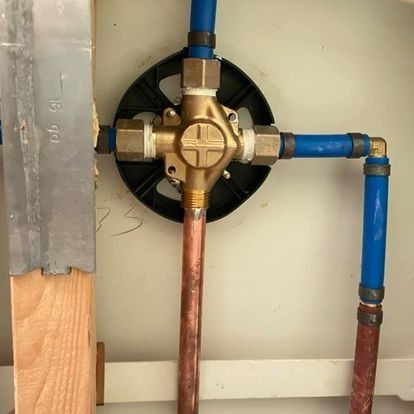 Plumbing fixture with copper and blue pipes, brass valve, black mounting bracket, mounted on wooden frame.