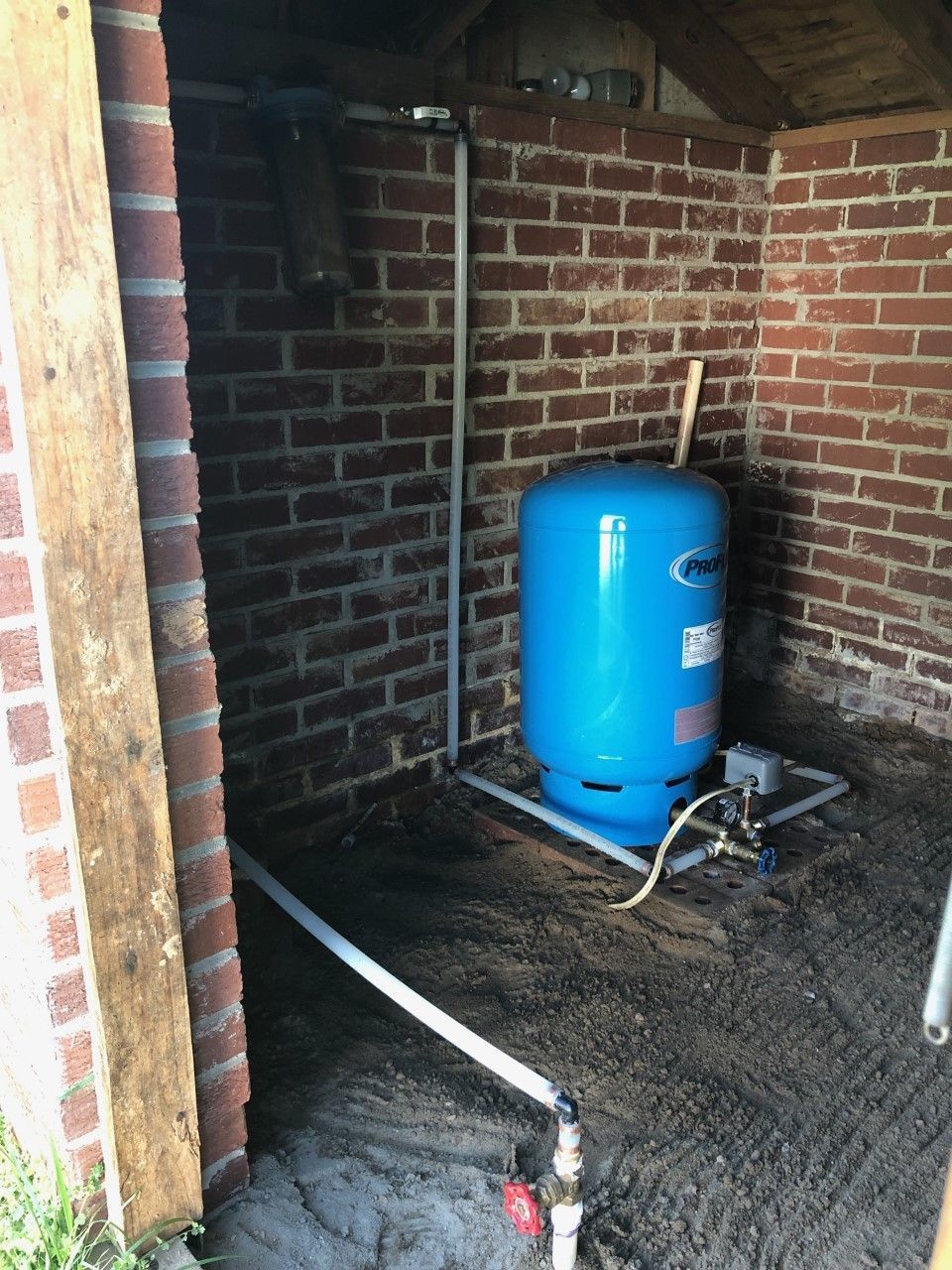 Blue water pressure tank in brick shed with exposed piping.