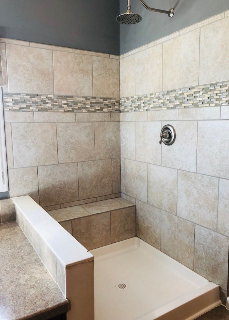 Tiled shower with a white basin and built-in bench. Features a decorative tile strip and a chrome shower head and faucet.