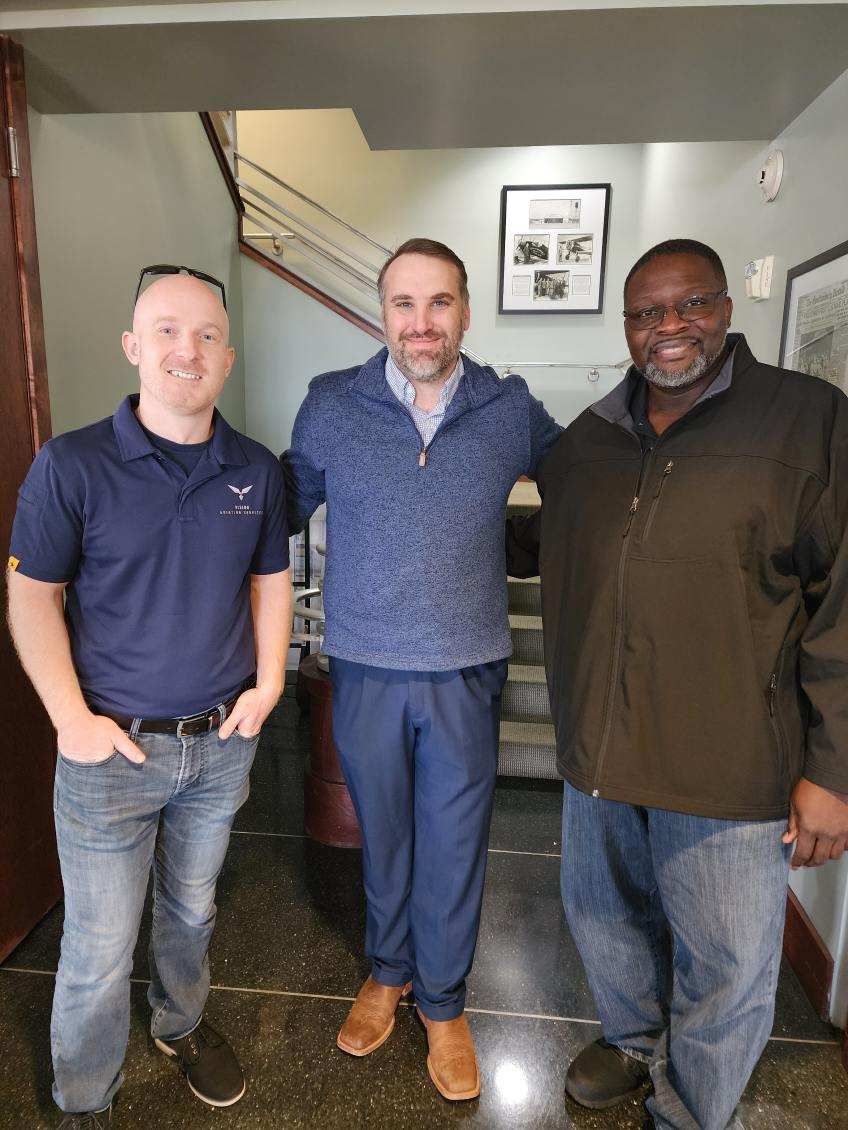 Three men are posing for a picture in a hallway.