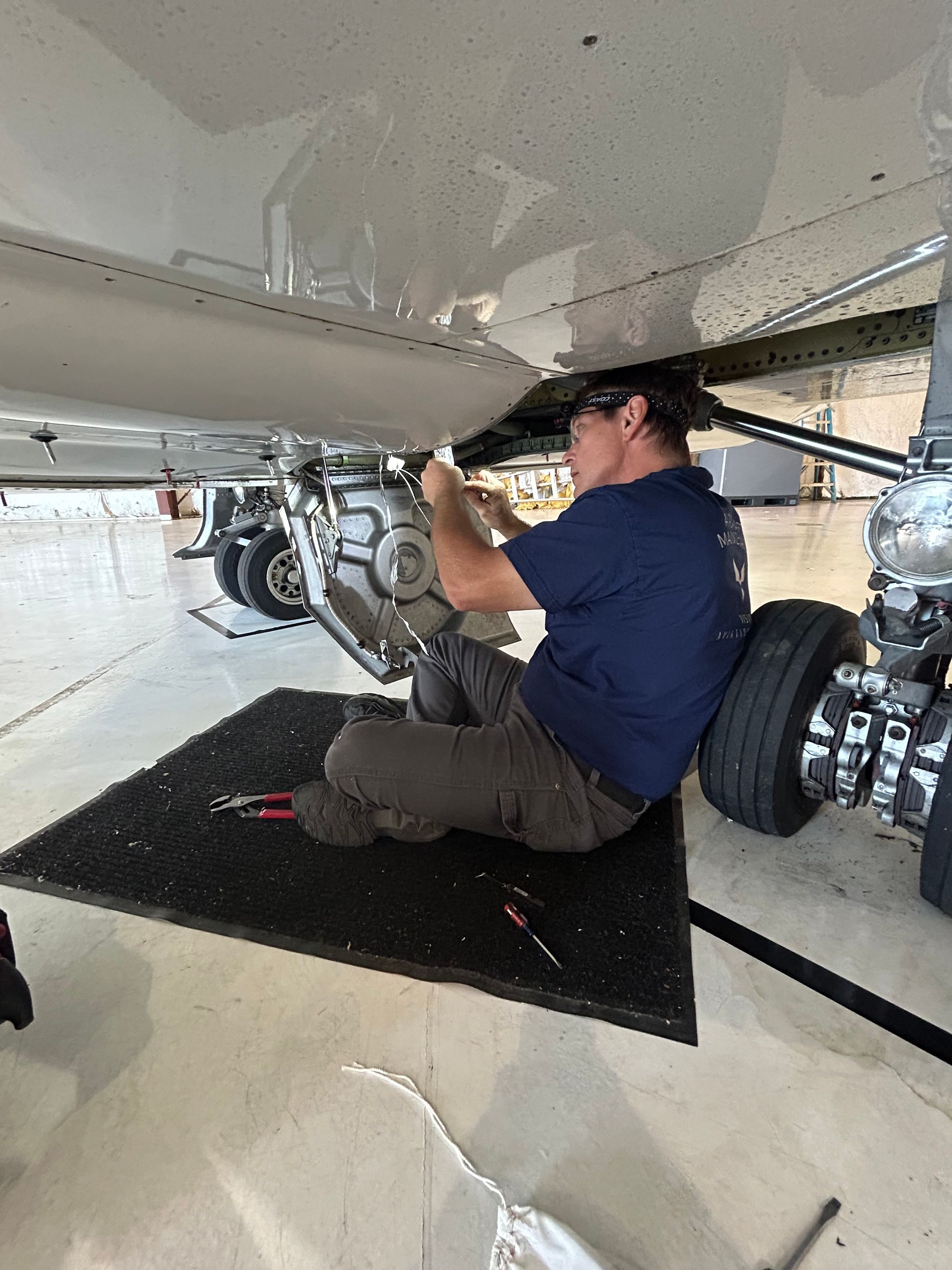 A man is working on the underside of an airplane in a hangar.