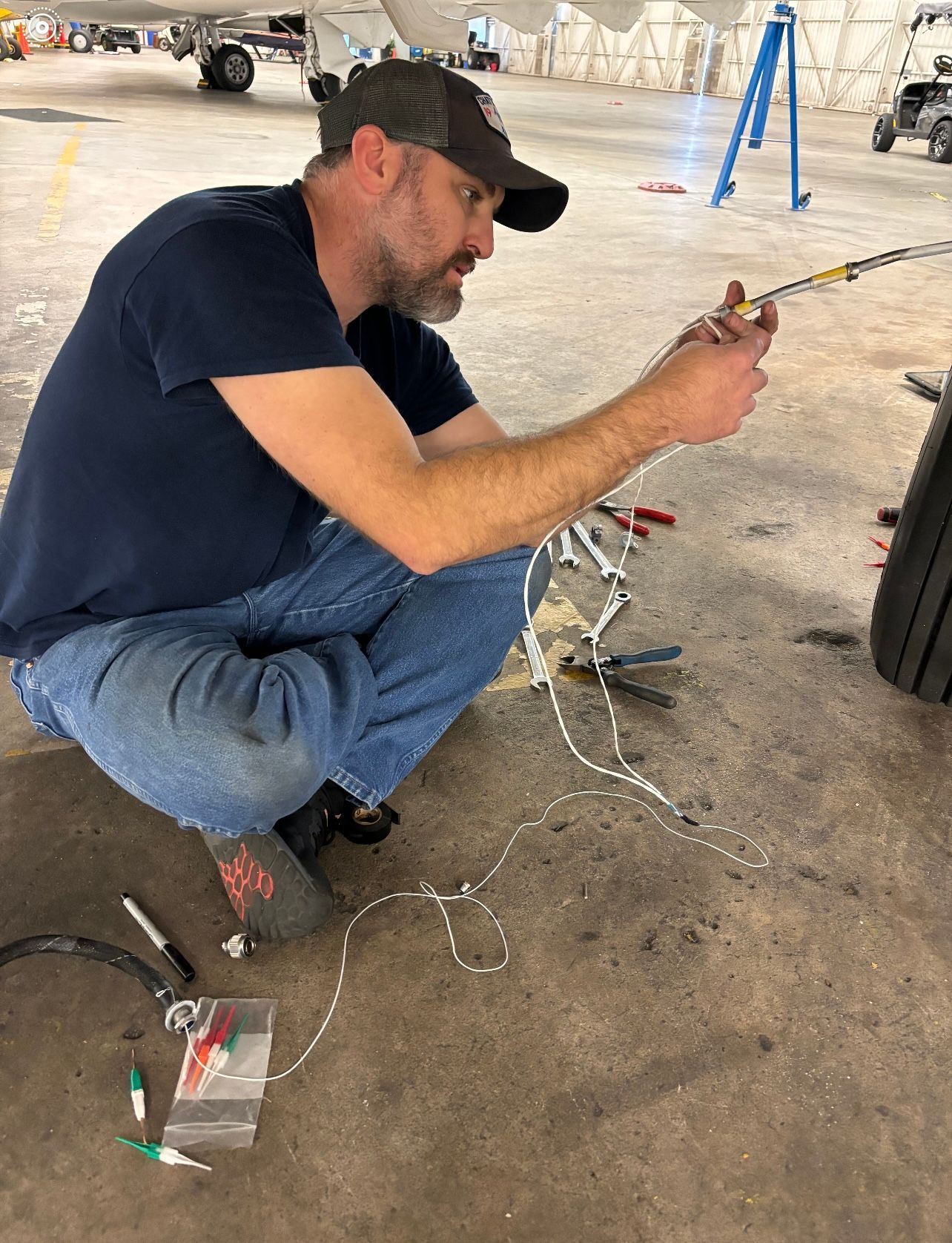 A man is kneeling down in a hangar working on a piece of equipment.