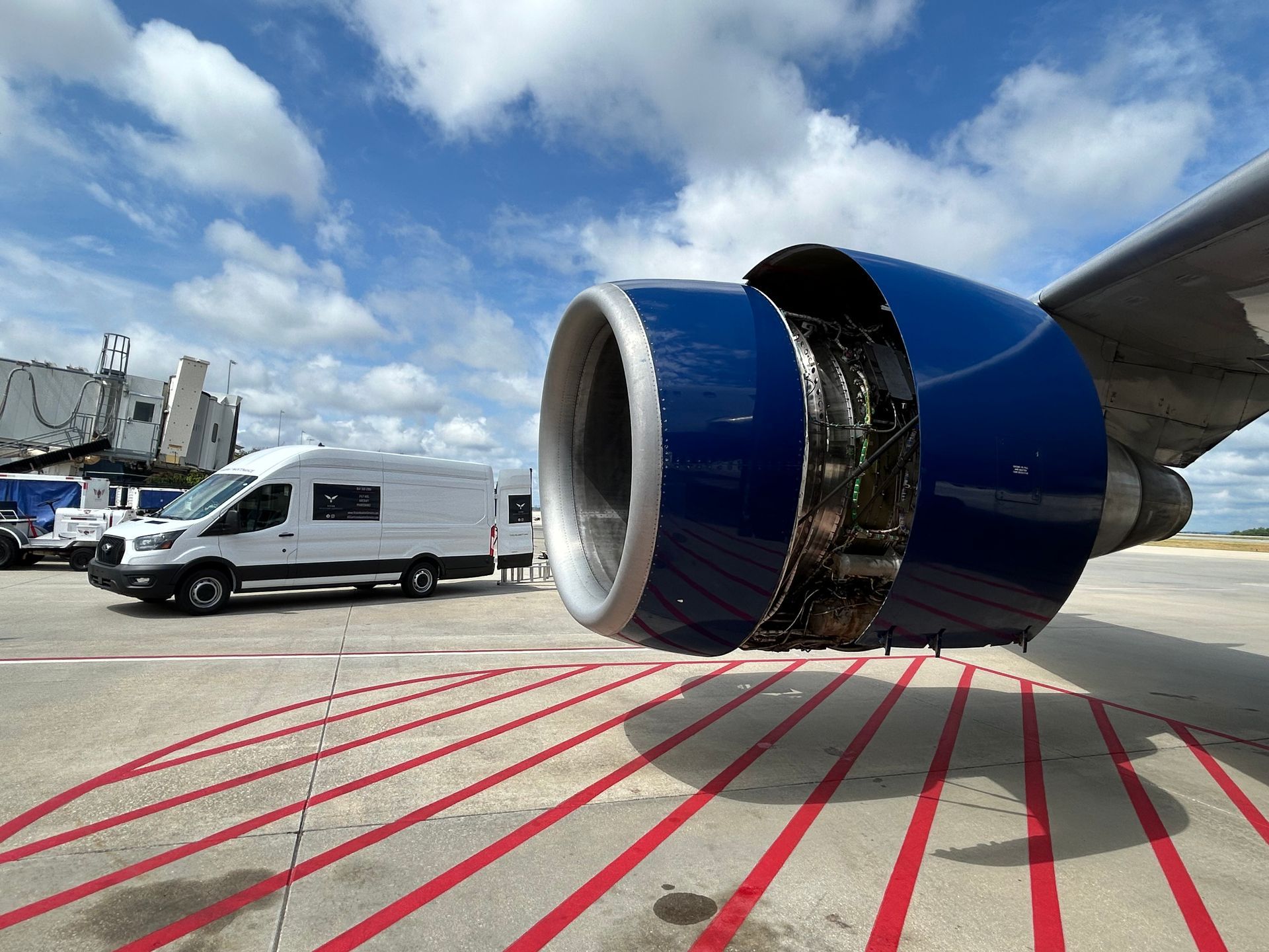 A large blue airplane engine is sitting on a runway next to a white van.