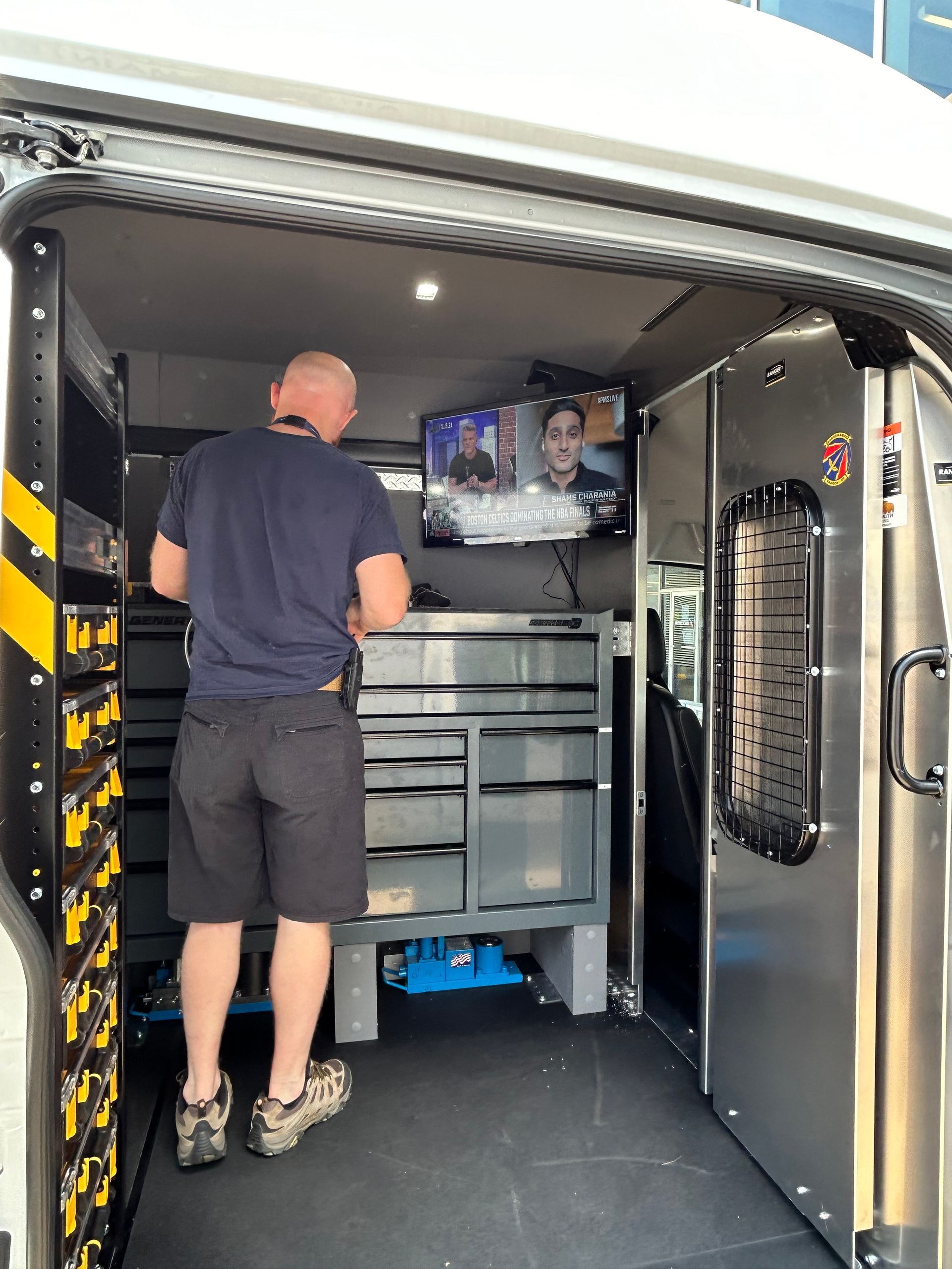 A man is standing in the back of a van with a tv on the wall.