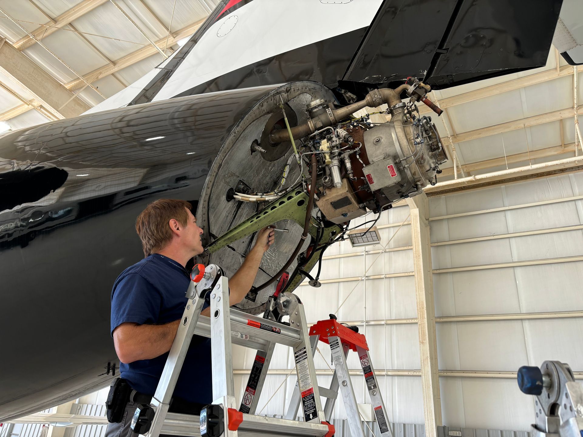 A man is standing on a ladder working on an airplane in a hangar.