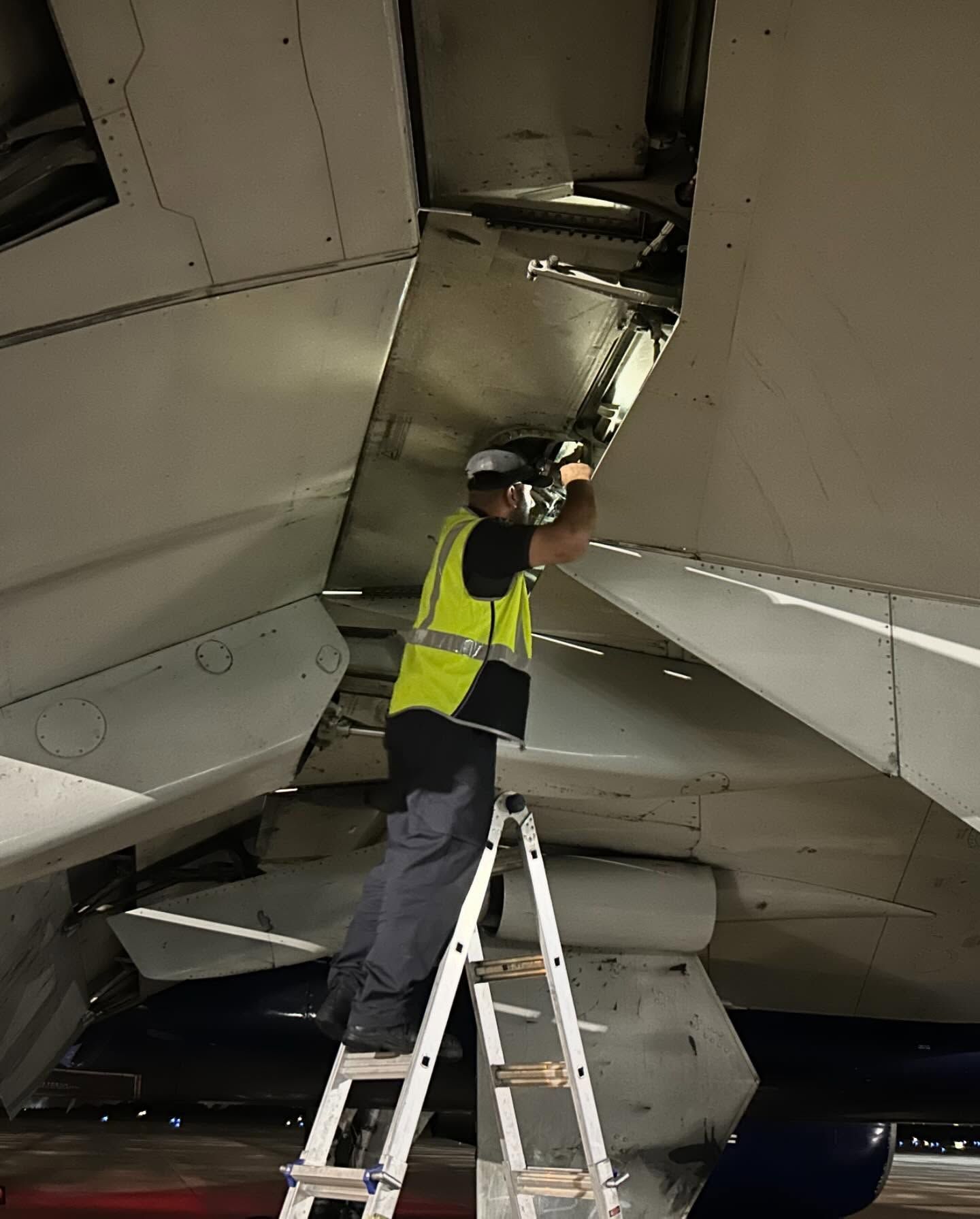 A man is standing on a ladder underneath an airplane.