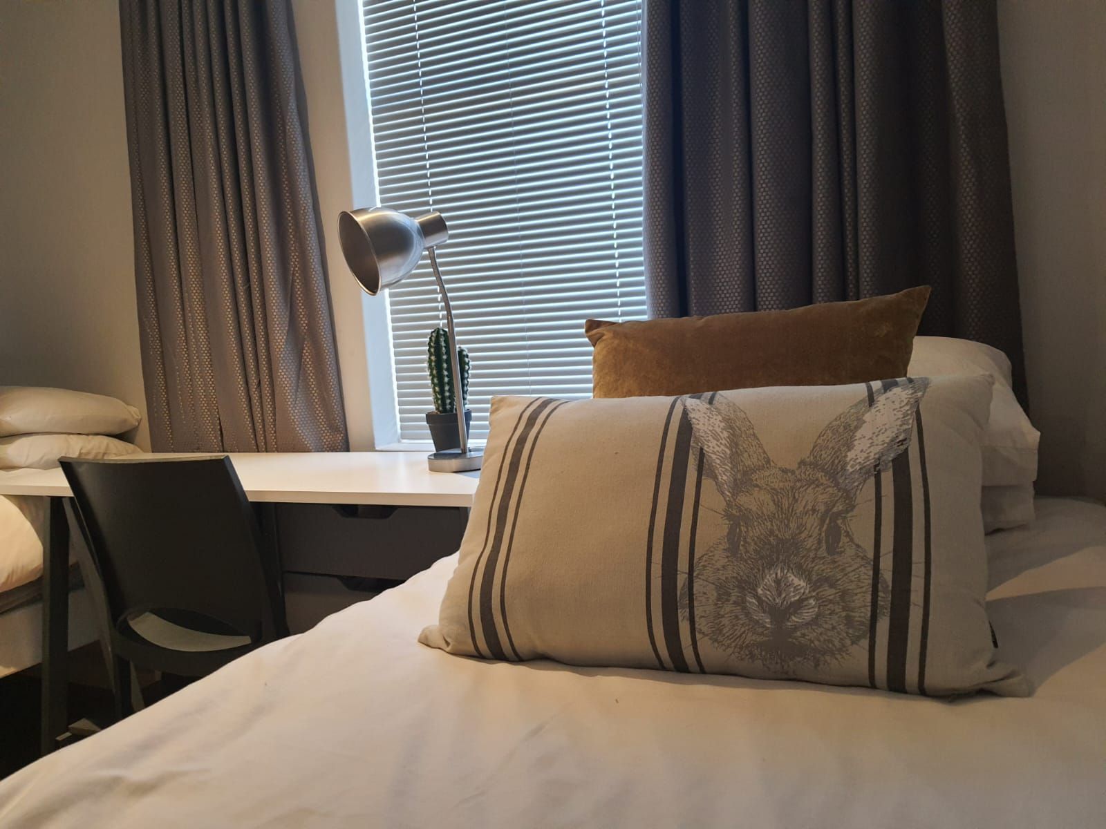 A bedroom with a bed , desk , chair , lamp and window.