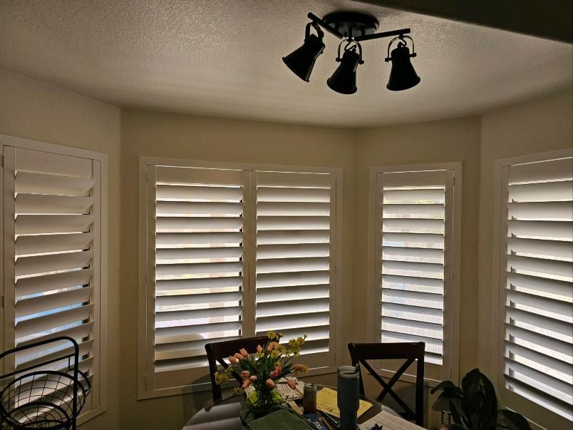 A dining room with a table and chairs and shutters on the windows.