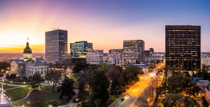 City skyline at dusk with illuminated buildings, a glowing dome, and tree-lined streets.