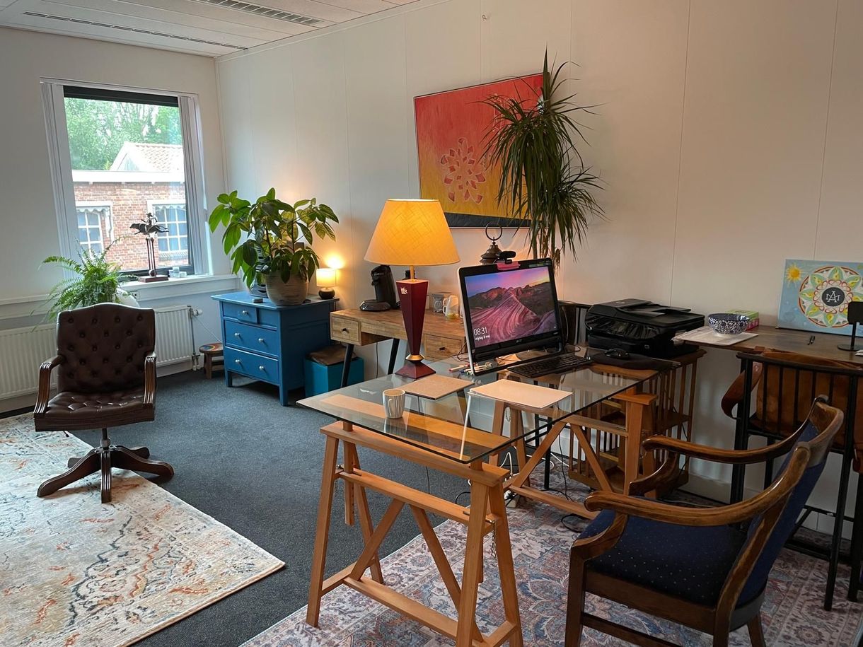 Thuiskantoor met bureau, lamp, planten, stoel en computer bij een licht raam.