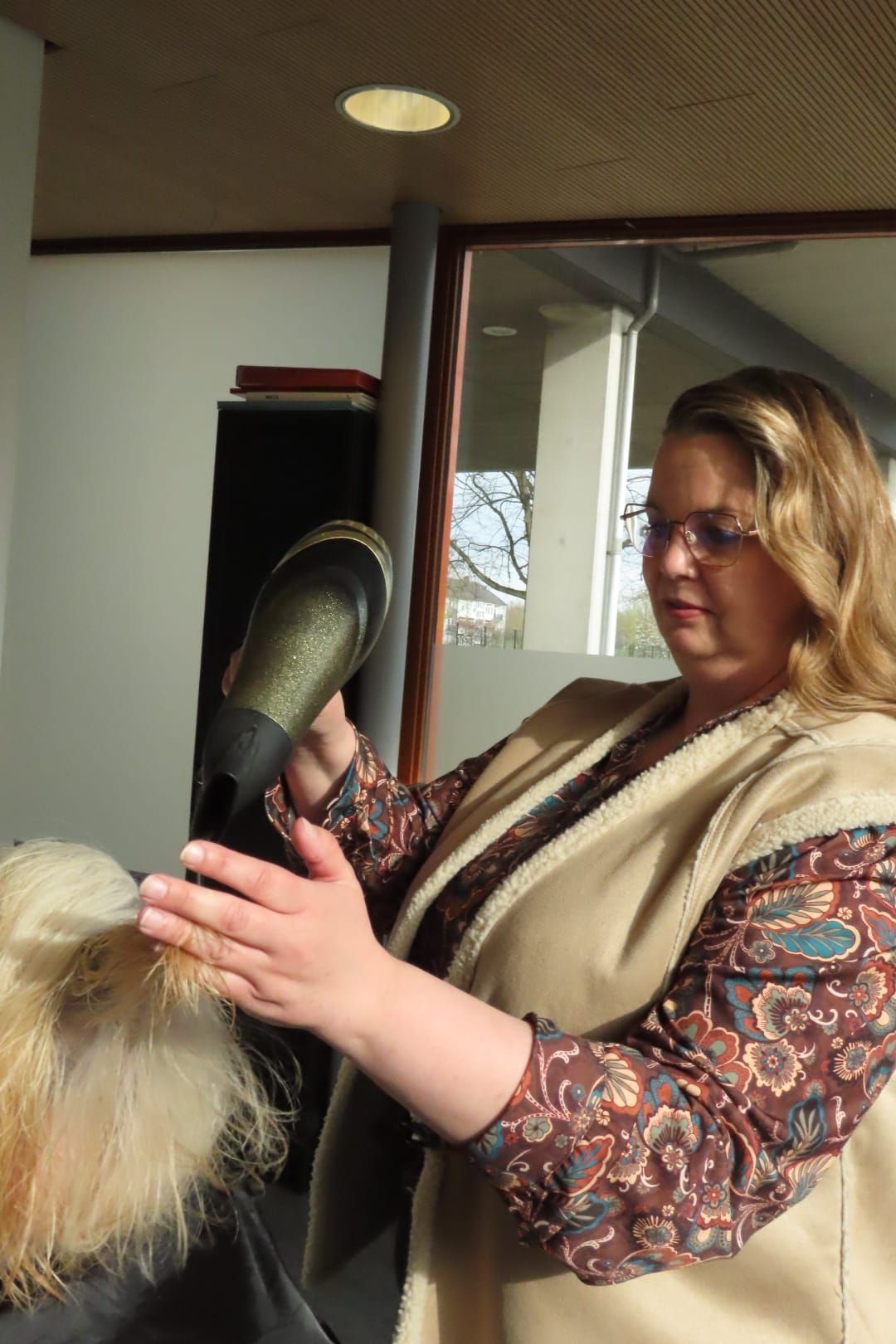Een vrouw in een kamer stylet een paspop met een blonde pruik.