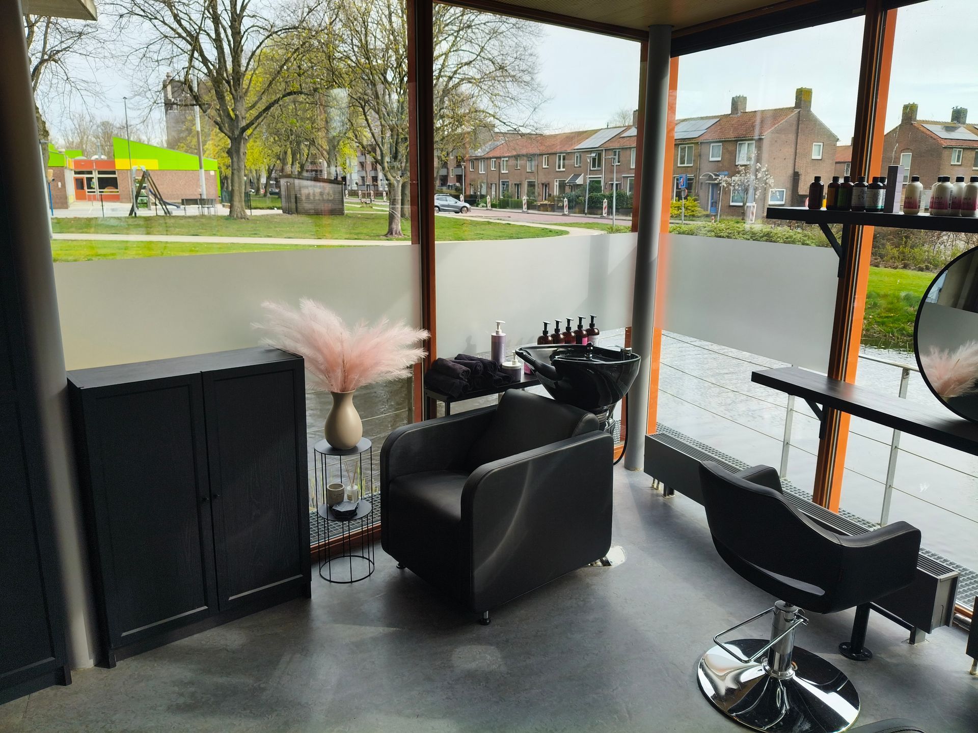Modern saloninterieur met zwarte kappersstoelen, spiegels en grote ramen aan de voorzijde met uitzicht op de straat.