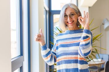 A woman in a striped sweater is giving a thumbs up sign.