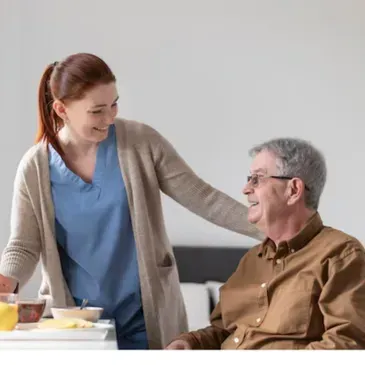 A woman is standing next to an older man sitting at a table.