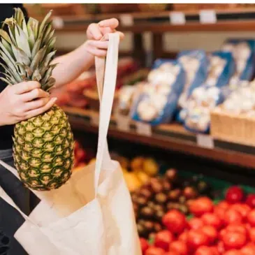 A person is holding a pineapple in a bag in a grocery store.