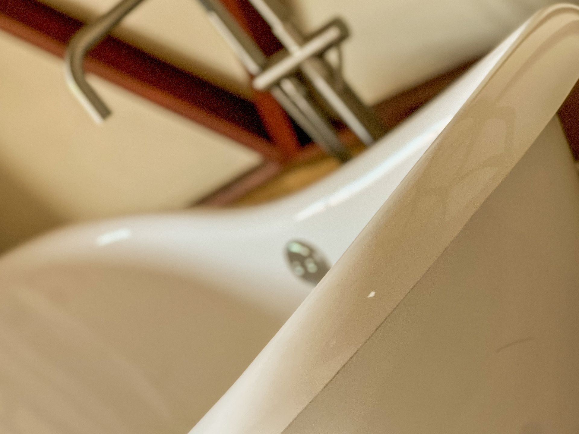 Detalhe da borda branca de uma pia com uma torneira de metal ao fundo.