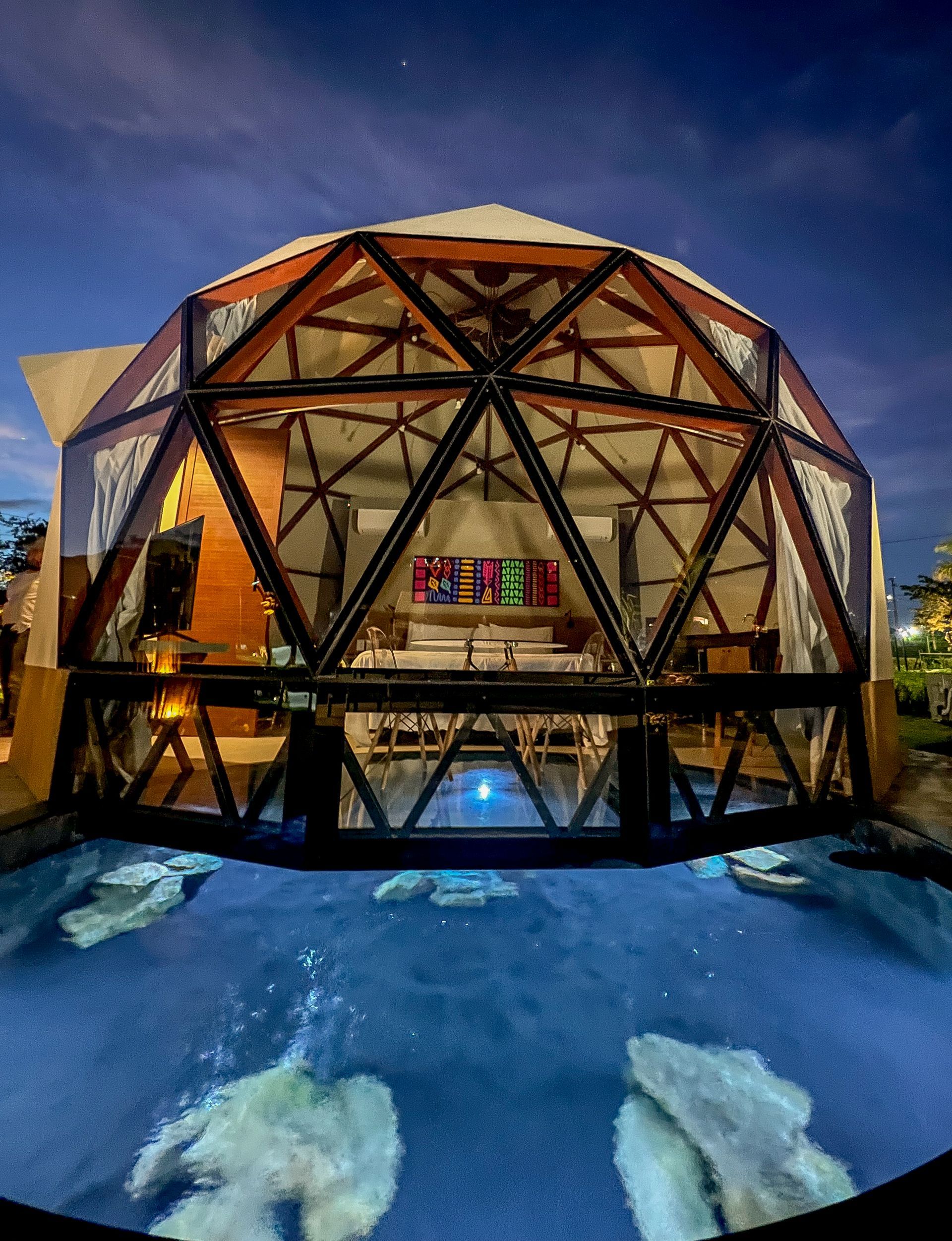Cúpula geodésica iluminada à noite ao lado de uma piscina azul com duas estátuas de ursos polares brancos.