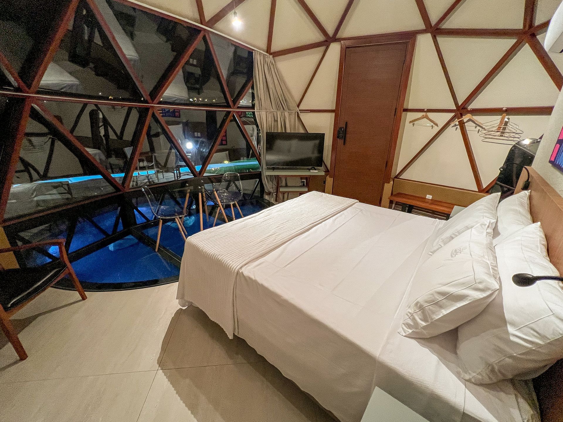 Quarto dentro de uma cúpula geodésica com cama, escrivaninha e grandes janelas com vista para o mar azul e as montanhas.