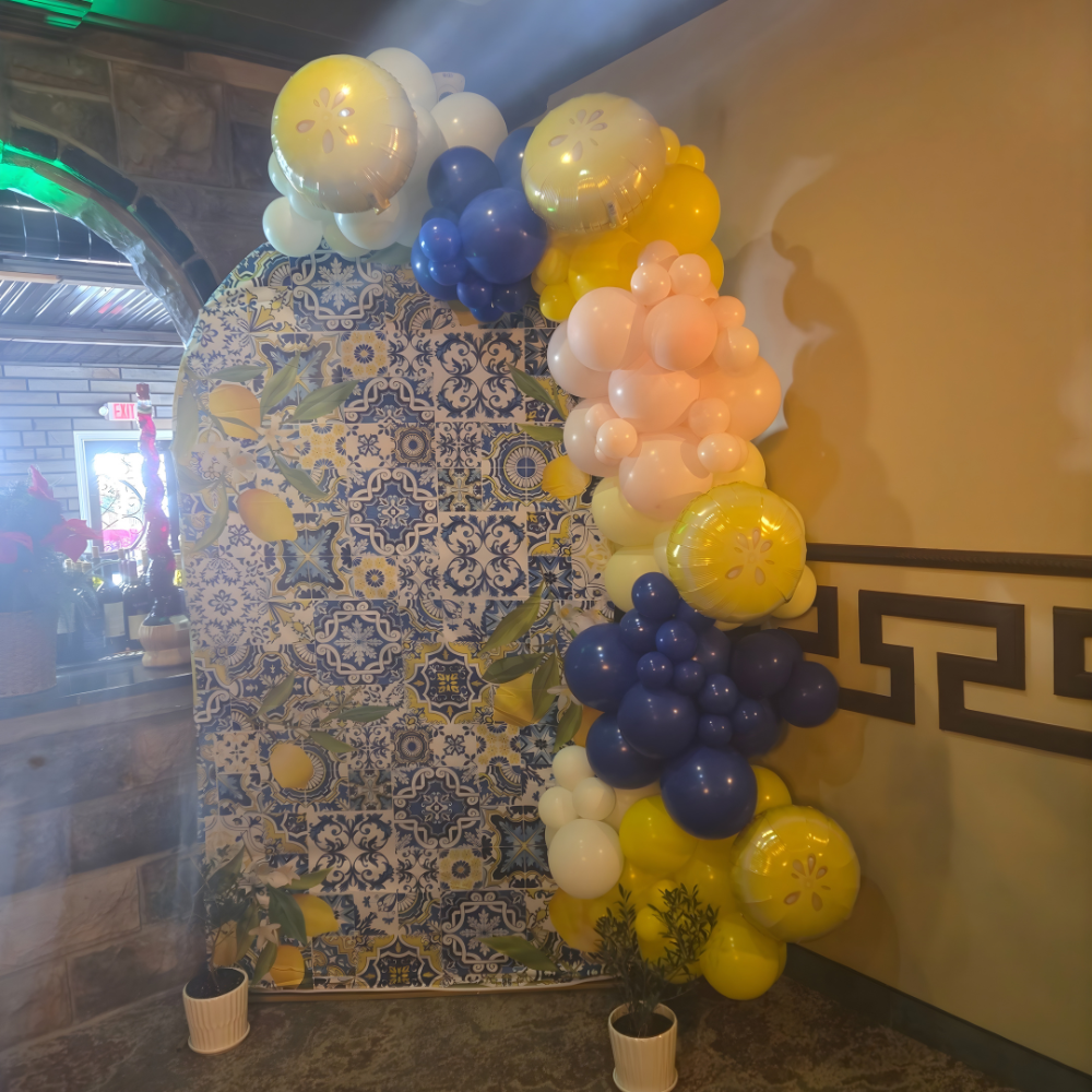 Balloon arch in yellow, white, and blue next to a patterned backdrop with lemons and tiles.