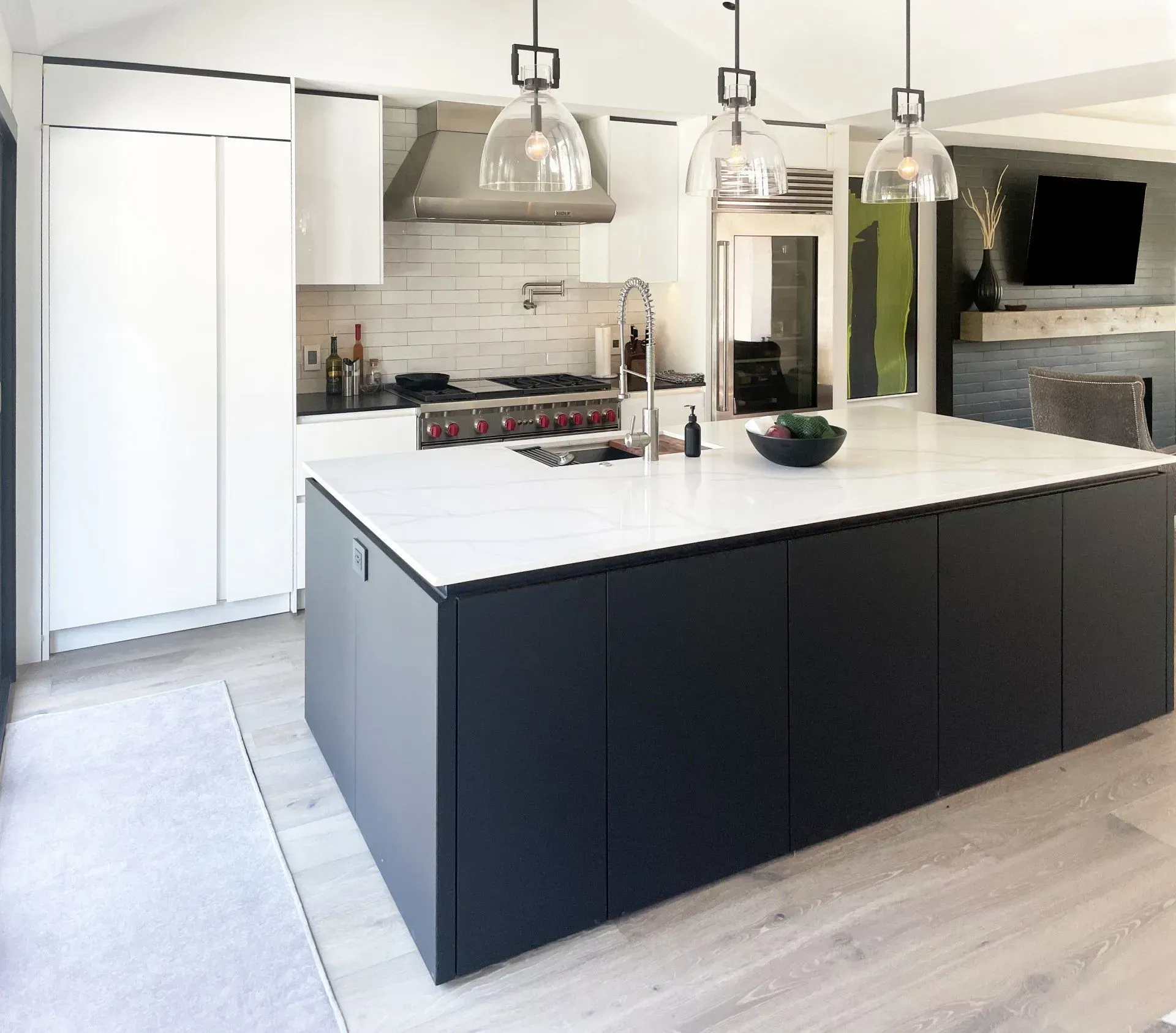 Modern kitchen with dark island, white countertops, stainless steel appliances, and light wood floors.