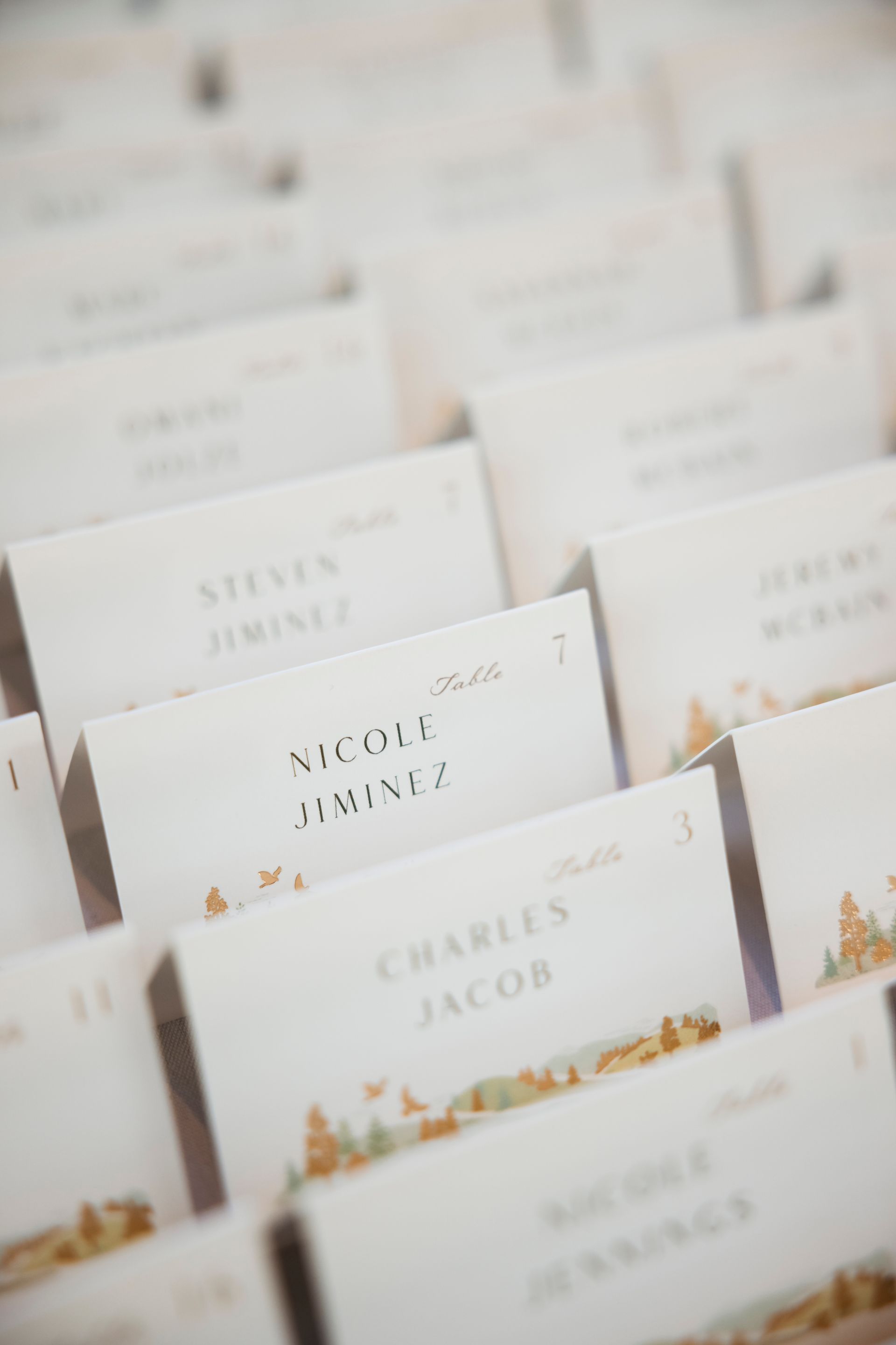White place cards with gold floral accents arranged in rows on a table