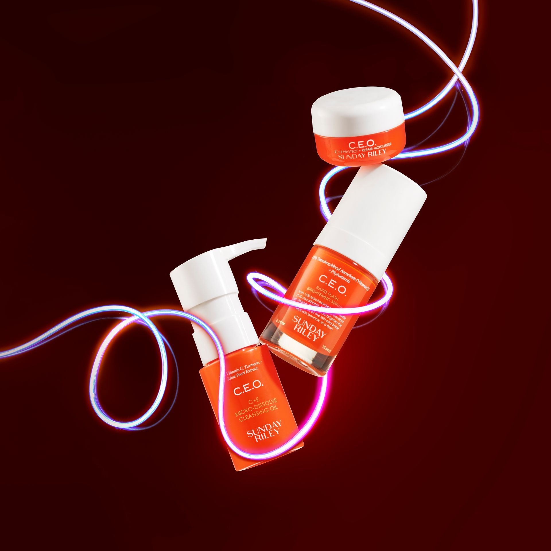 Three orange cosmetic bottles with white caps wrapped in glowing pink light on a dark red background