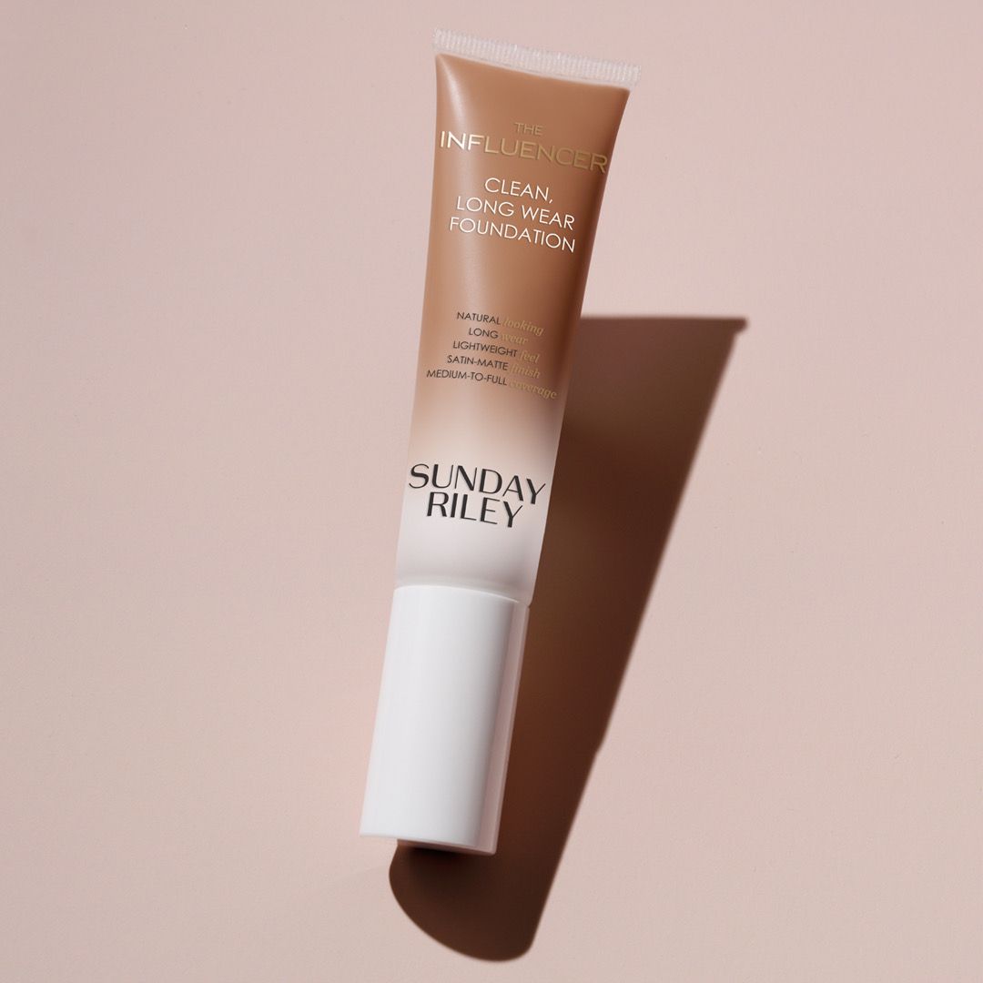 Beige skincare tube with white cap, standing on a soft pink background with a long shadow