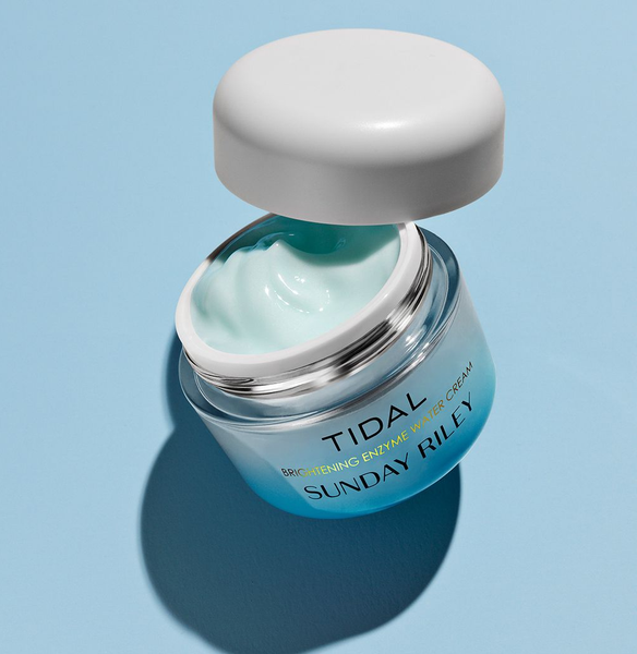 Open jar of light blue cream with white lid on a blue background