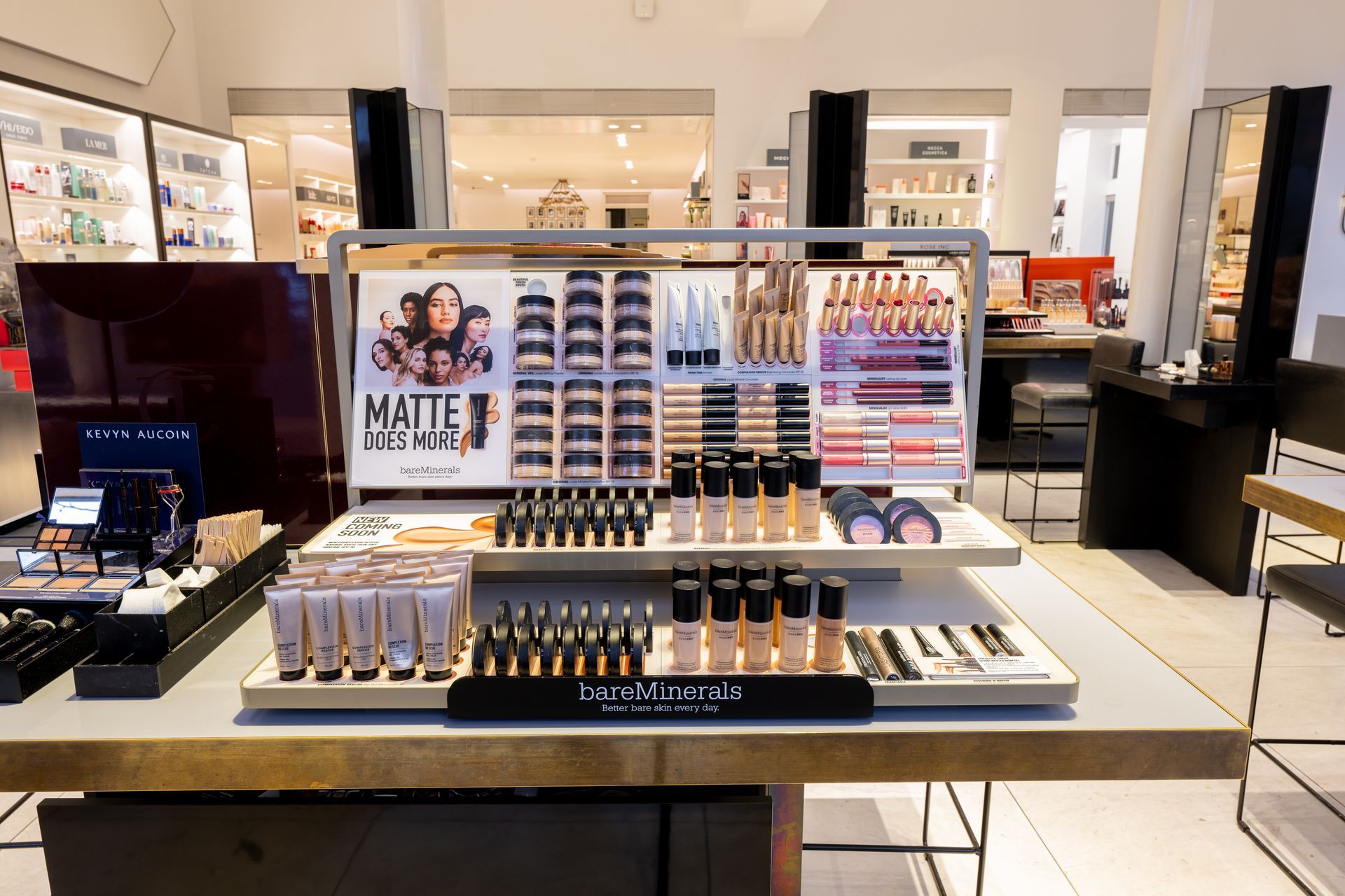 Cosmetics display counter with makeup palettes, lipsticks, and nail products in a bright store.