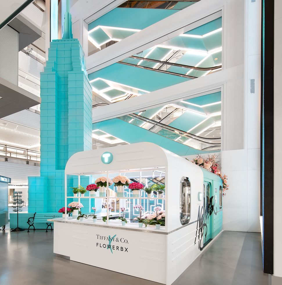 Bright turquoise atrium with a small white kiosk and floral displays in a modern shopping mall