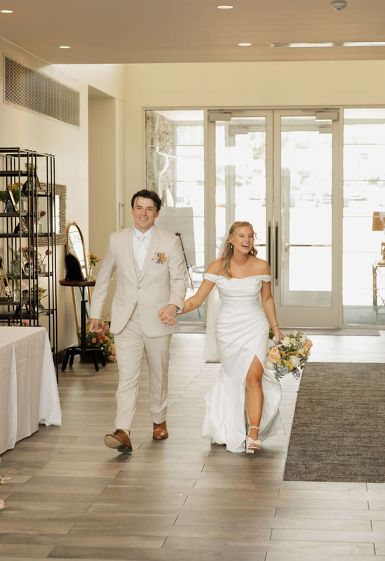 Bride and groom walking hand in hand down a bright hallway, bride holding a bouquet