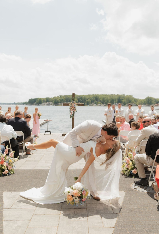 Bride and groom kissing at waterfront wedding ceremony with guests seated nearby