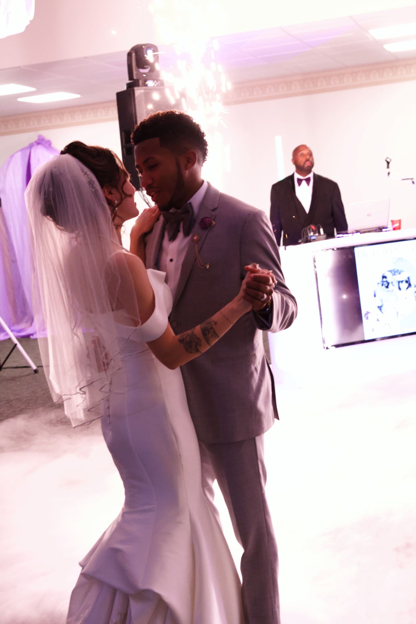 Bride and groom slow dancing at a wedding reception with a DJ in the background