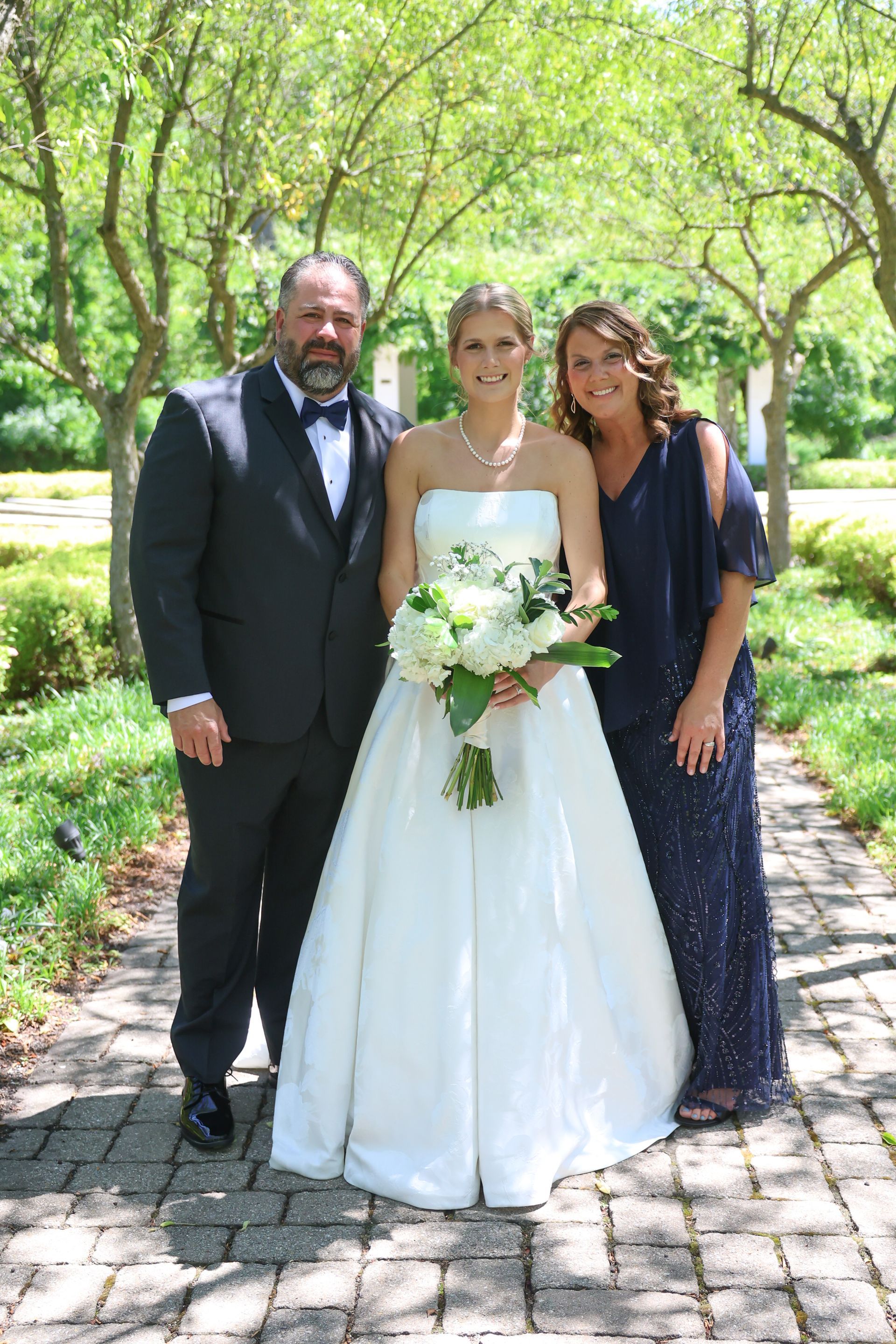 Bride and parents standing outdoors in a park