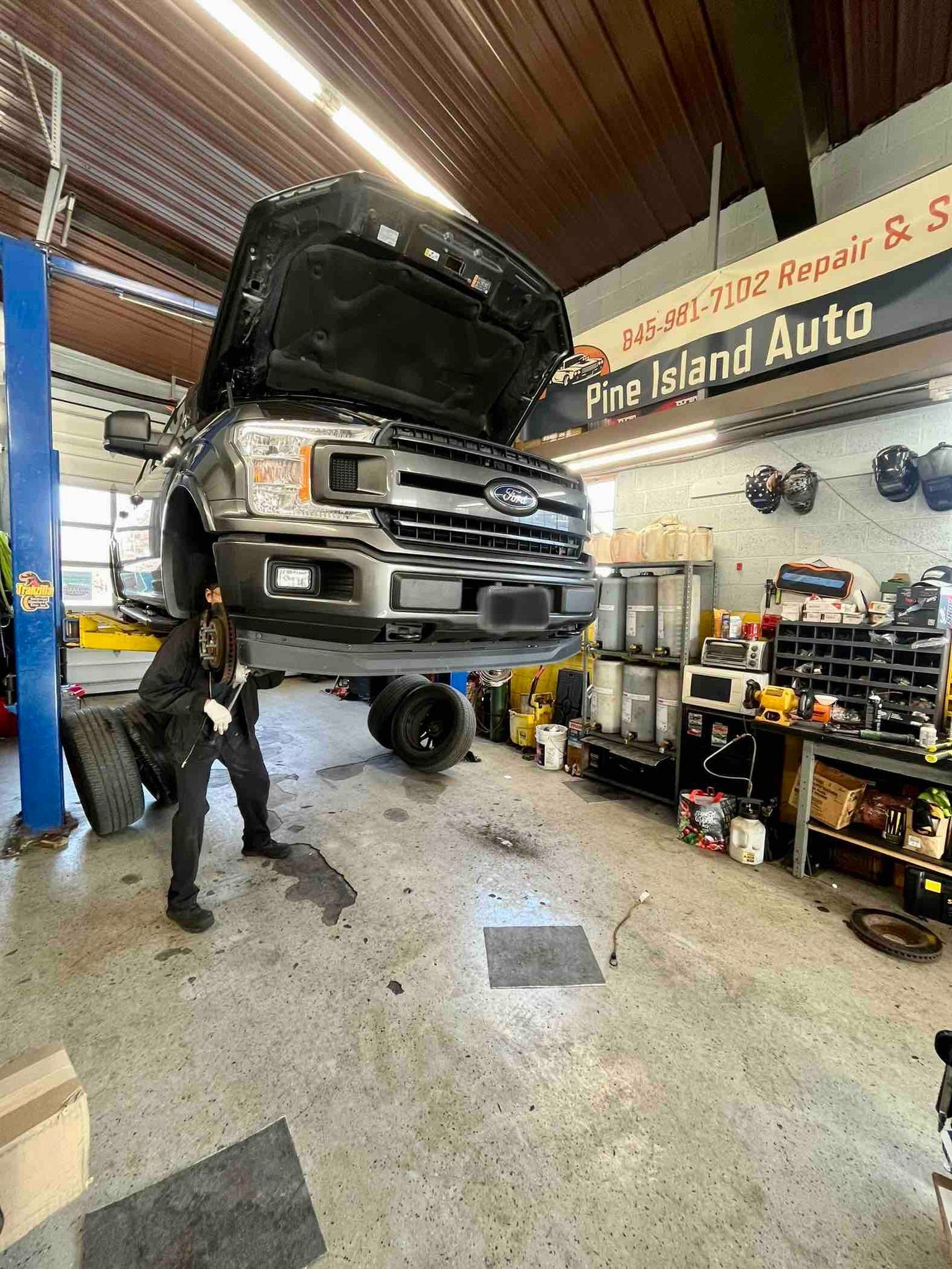 Truck on a lift at Fire Island Auto. Mechanic working under the vehicle in a garage setting.