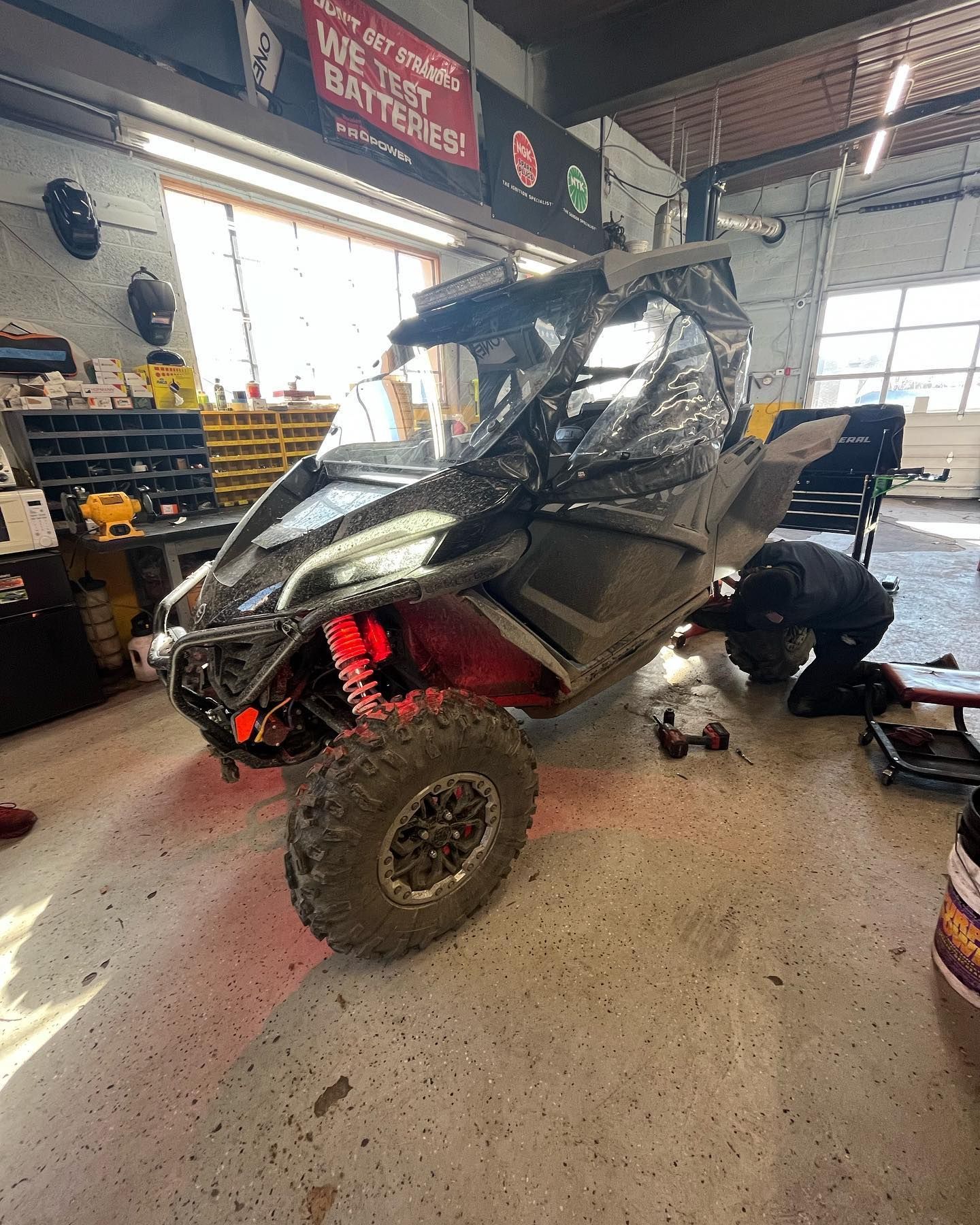 Black UTV with red suspension in a garage, a person works on it.