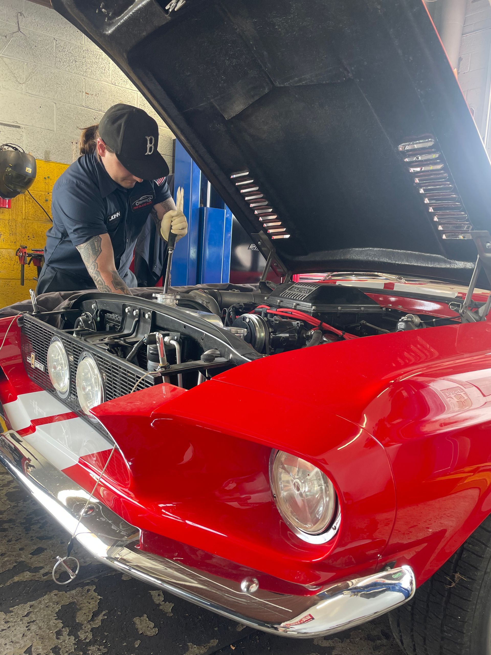 Mechanic working on the engine of a red classic car with open hood; garage setting.