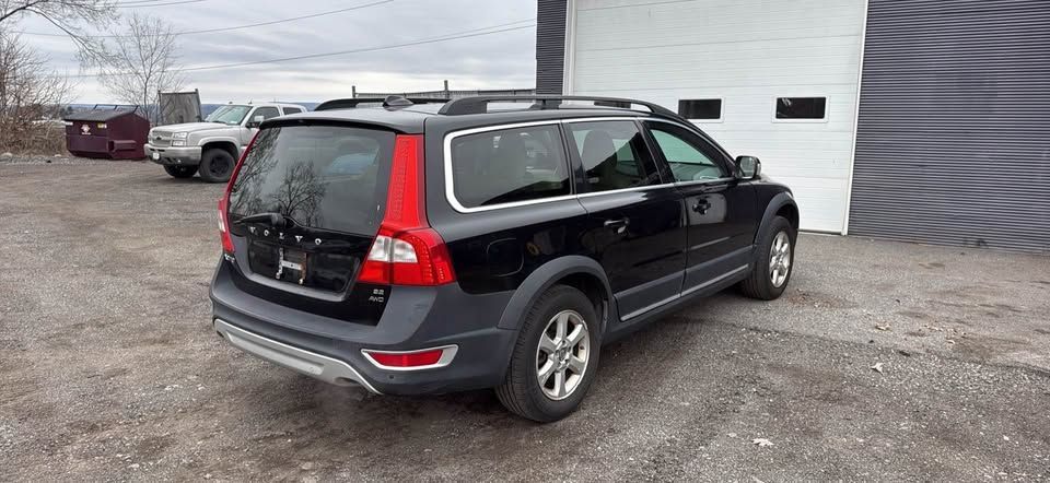 A black Volvo XC70 station wagon parked on a gravel lot in front of a white building.